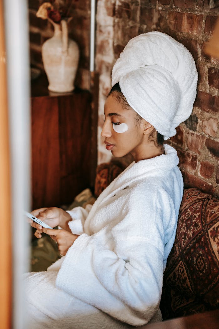 Ethnic woman in robe surfing internet on smartphone in salon